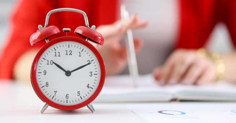 Red alarm clock sits in front of a person writing last-minute year-end fundraising outreach