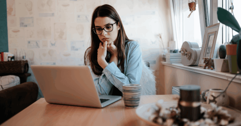 A professional young woman sits at a laptop with a worried look on her face, perhaps concerned about a summer slump.