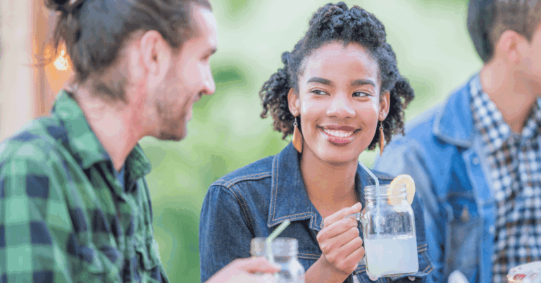 Young woman smiling while holding a glass of lemonade in this header for a blog about summer fundraiser ideas.