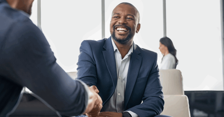 Business man wearing a suit jacket smiles as he shakes a colleague's hand, aiming to build donor trust