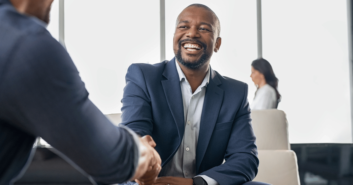 Business man wearing a suit jacket smiles as he shakes a colleague's hand, aiming to build donor trust