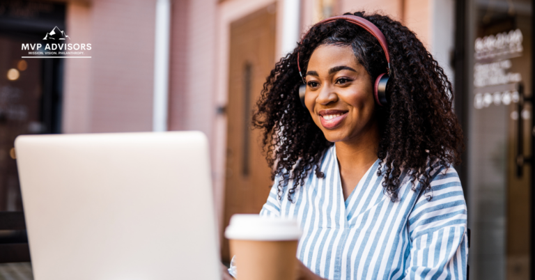 Woman wears headphones and smiles while working on recurring donations on a computer