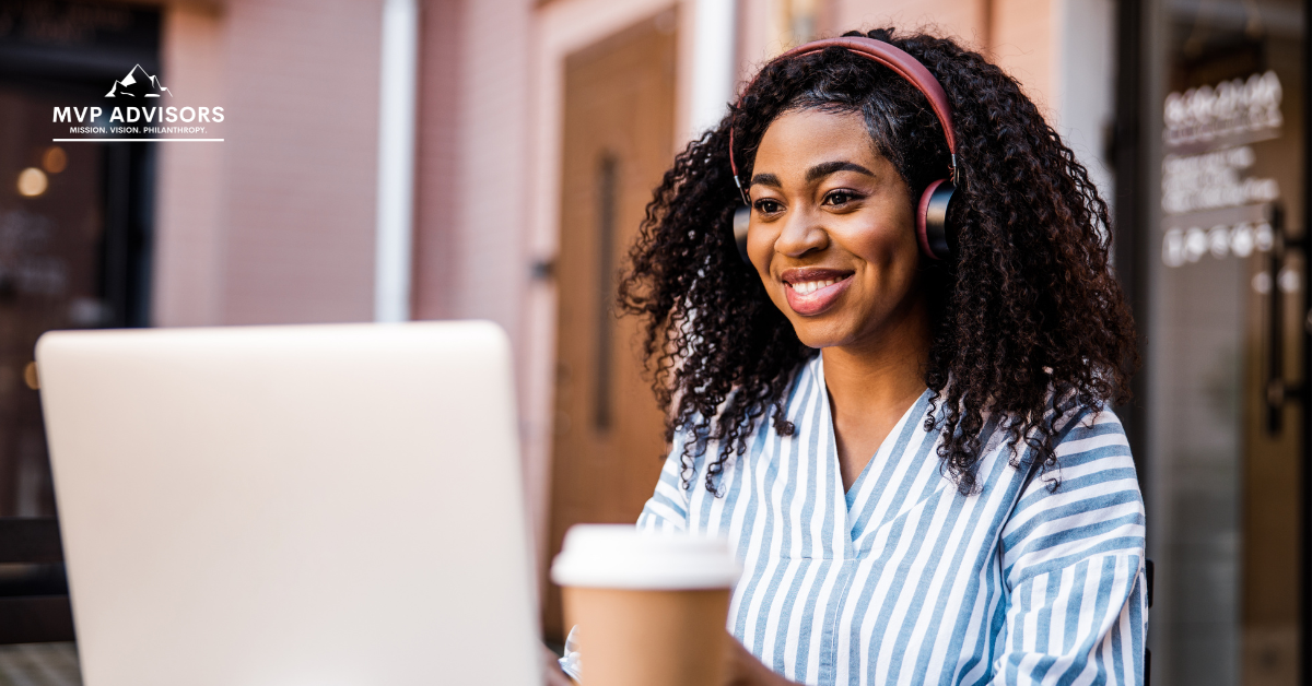 Woman wears headphones and smiles while working on recurring donations on a computer